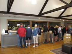 The bar at Cloudy Bay Vineyards, Marlborough, sits in front of wall of windows with a view of a cellar full of wine barrels.